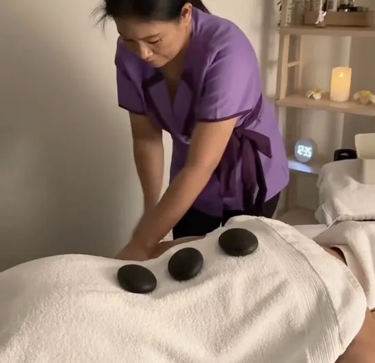 Suw placing warm stones along a client's back