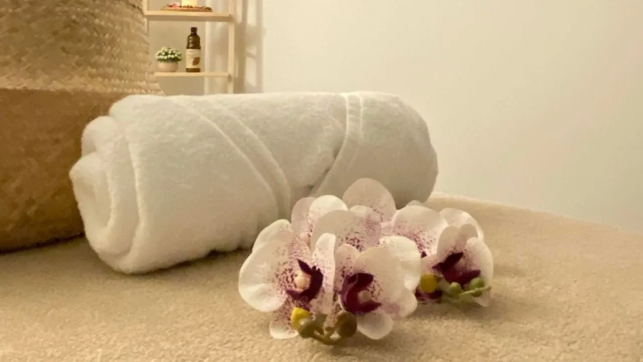 A rolled white towel and orchids on a massage table at Lux Thai